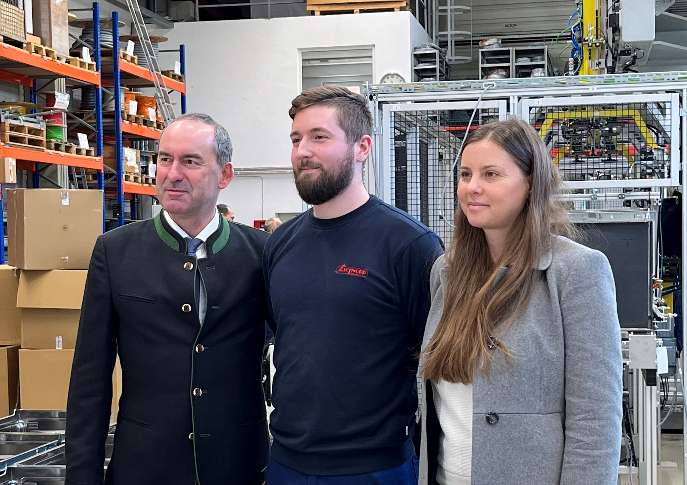 Bayerns Wirtschaftsminister Hubert Aiwanger mit der Geschäftsführenden Gesellschafterin Carmen Schnupp und einem Mitarbeiter der Schnupp GmbH. & Co. Hydraulik KG. Schmuckbild Hubert Aiwanger steht im Bild Links mit einem Mann und einer Frau in einer Arbeitshalle mit Regalen